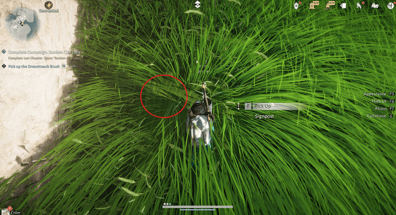 The brush is in the grass beside the pale wall.